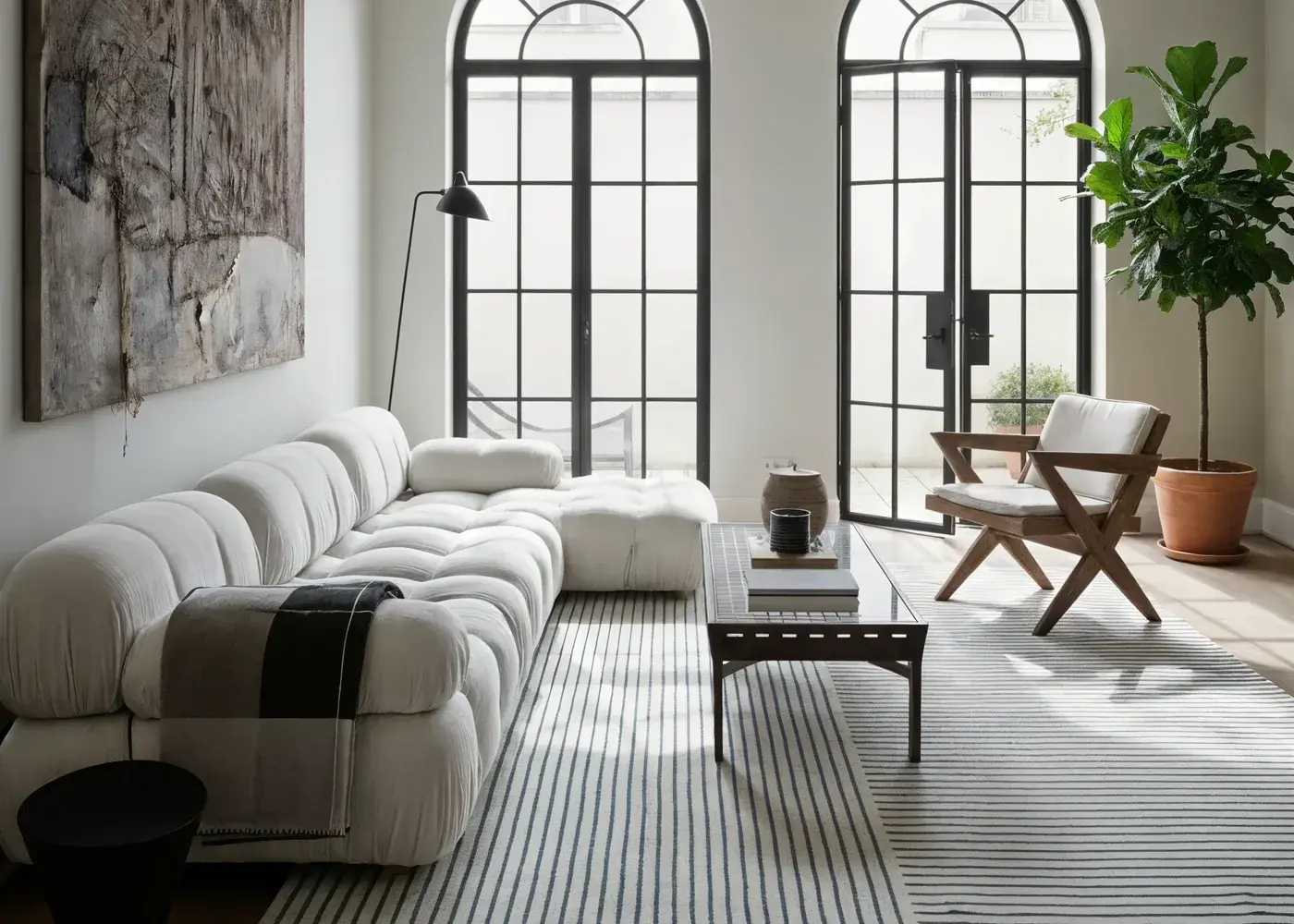 The Eucalyptus rug, fine pale stripes, under a bouclé sofa in a room with tall arched windows